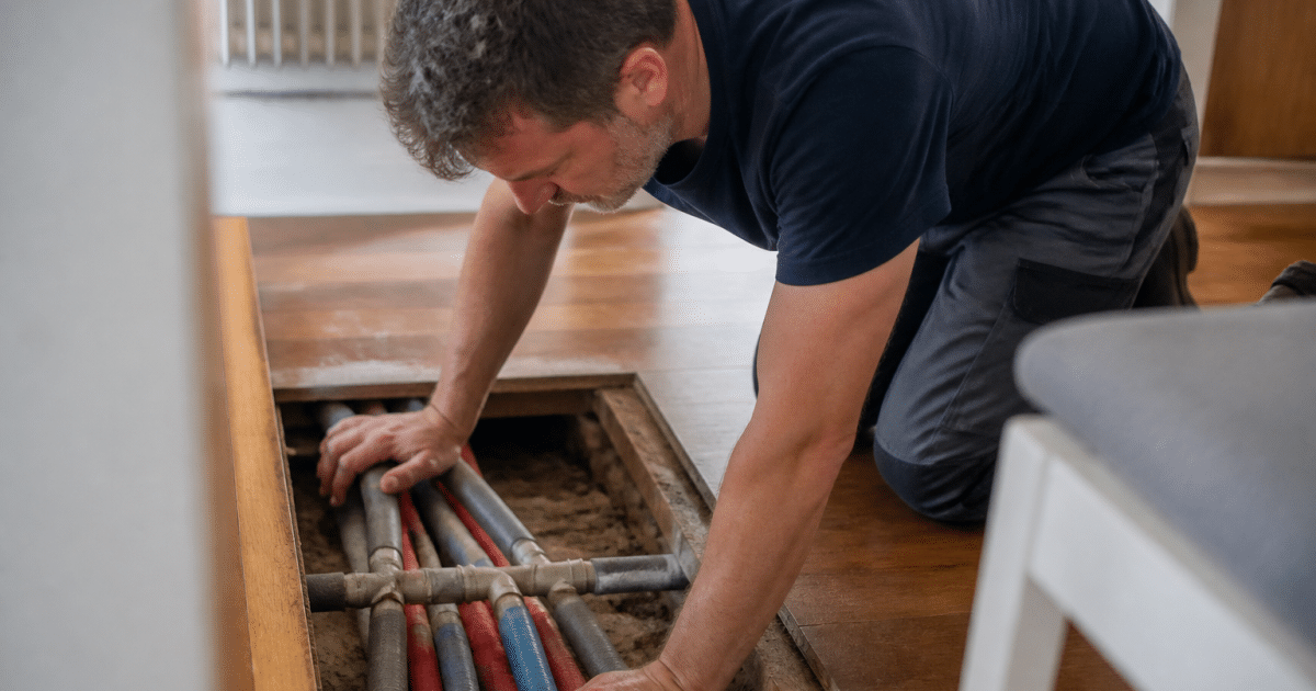 Technicien inspecte tuyaux chauffants sous plancher ouvert