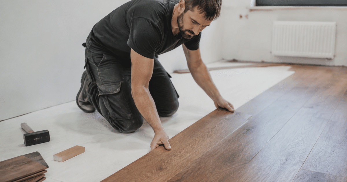 Ouvrier posant des lames de parquet brun sur sol blanc
