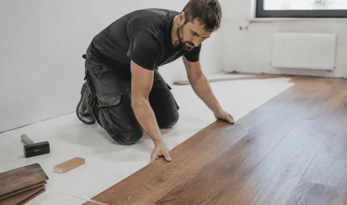 Ouvrier posant des lames de parquet brun sur sol blanc