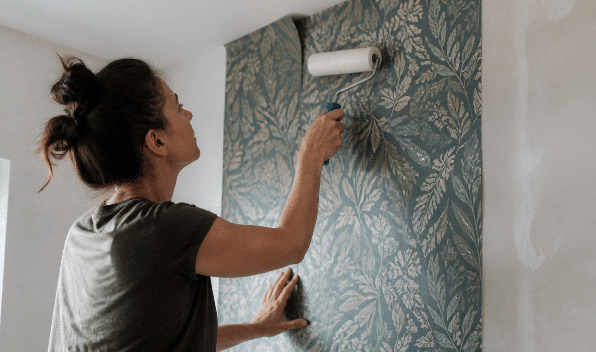 Personne appliquant papier peint sur mur avec rouleau