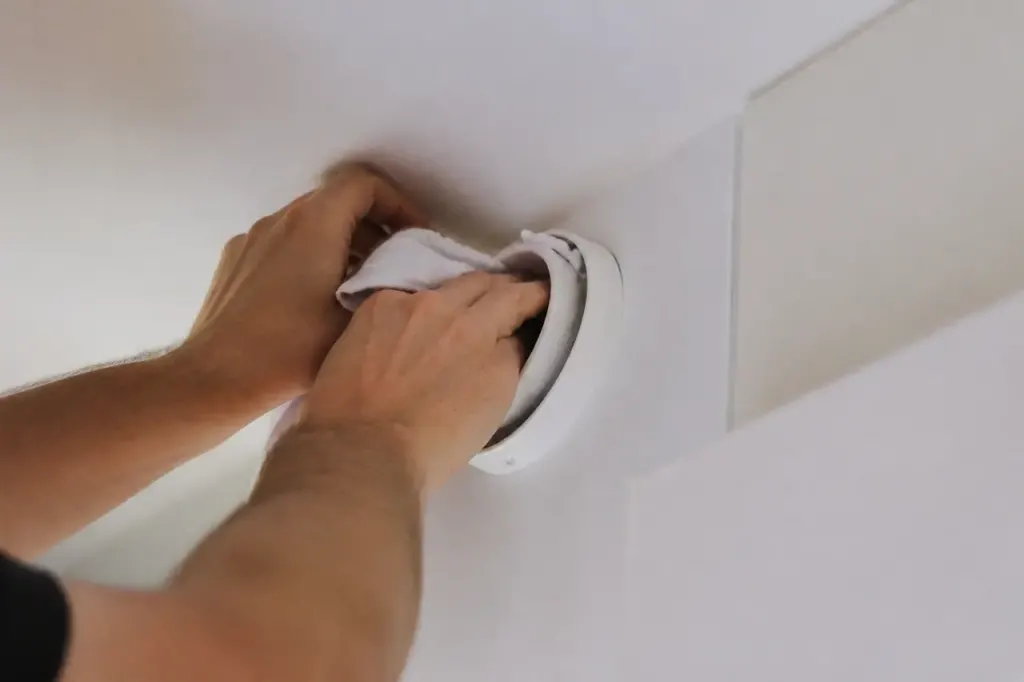 Mains nettoyant une bouche de VMC avec chiffon blanc